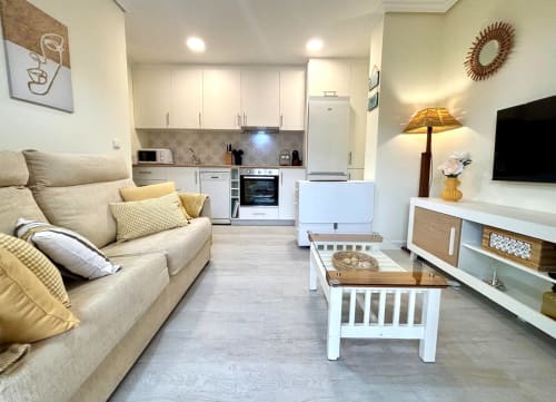 Acogedor apartamento Luceira en Baiona con sofá beige, cocina moderna, TV de pantalla plana y mesita blanca.