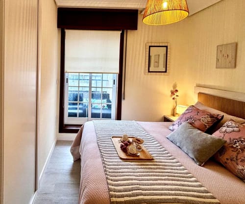 Acogedor dormitorio del apartamento Luceira en Baiona con vistas al mar, ropa de cama a rayas, cabecero de madera y acceso a balcón