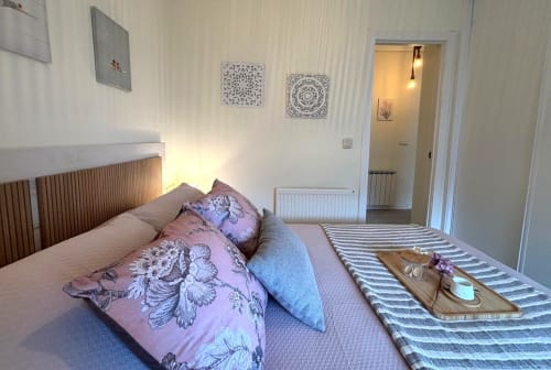 Dormitorio luminoso en apartamento de Baiona con ropa de cama estampada rosa, cabecero de madera y acceso a vista al mar por puerta de balcón