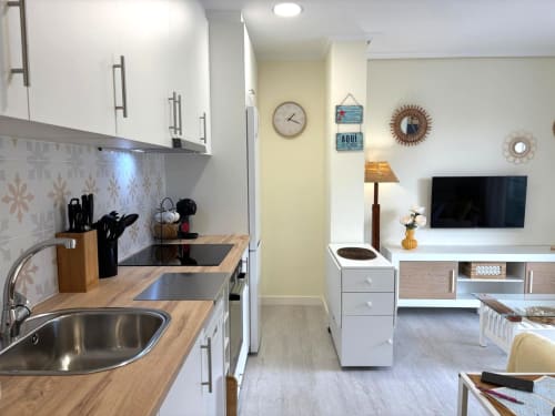 Moderna cocina y sala de estar en apartamento Luceira, Baiona con muebles blancos, encimeras de madera y electrodomésticos de acero inoxidable