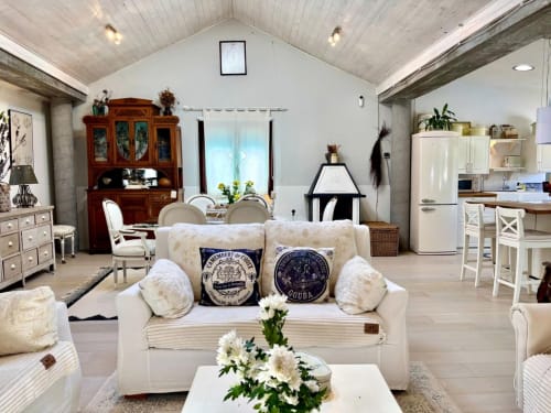 Luminoso salón diáfano con sofá crema, vigas vistas, cocina, comedor y chimenea en Baiona