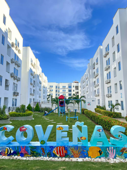 Colorido letrero COVEÑAS en el patio del hotel Olamar Living con apartamentos blancos, área de juegos y vista al jardín en Coveñas,