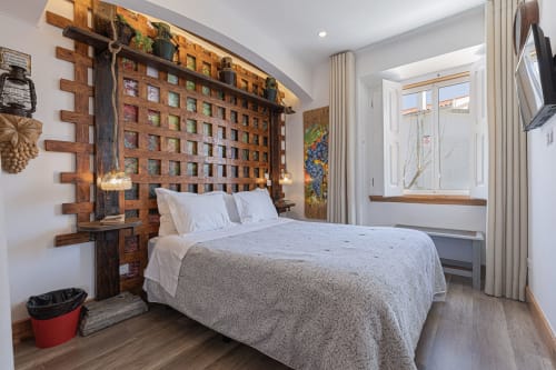 Modern Standard room at Ninho Saloio with wooden lattice headboard, gray bedding, white pillows, windows, wooden floors, and