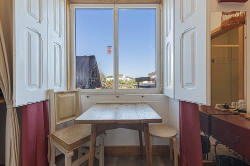 Standard room at Ninho Saloio with dining table, wooden chairs, and window overlooking Venda do Pinheiro