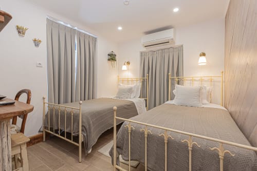 Two single beds with brass frames in a bright bedroom at Ninho Saloio hotel, Venda do Pinheiro, with grey curtains and modern