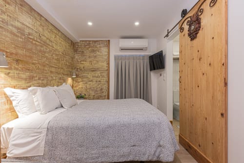 Cozy small hotel room at Ninho Saloio with brick accent wall, queen bed, wooden wardrobe, AC, TV, and modern amenities