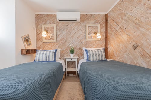 Cozy twin bedroom at Ninho Saloio with wooden herringbone walls, striped pillows, air conditioning, and brass wall sconces in