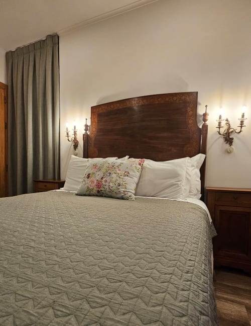 Elegant bedroom at Ninho Saloio with wooden headboard, white pillows, beige bedding, wall sconces, and gray curtains in Venda