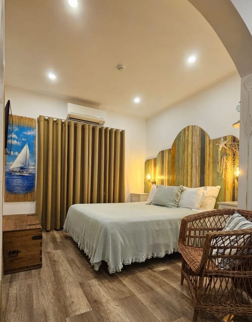 Seagull Studio bedroom at Ninho Saloio with queen bed, wooden headboard, gold curtains, wicker chairs, and hardwood floors.