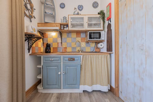 Cozy kitchenette in Seagull Studio at Ninho Saloio, featuring blue cabinets, wooden shelves, and nautical decor