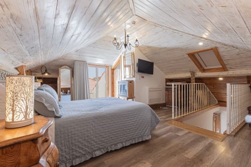 Spacious loft bedroom at Ninho Saloio with whitewashed ceiling, hardwood floors, queen bed, and city views from balcony