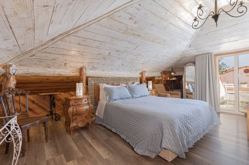 Rustic bedroom at Ninho Saloio with wooden beams, double bed, hardwood floors, and balcony view in Venda do Pinheiro