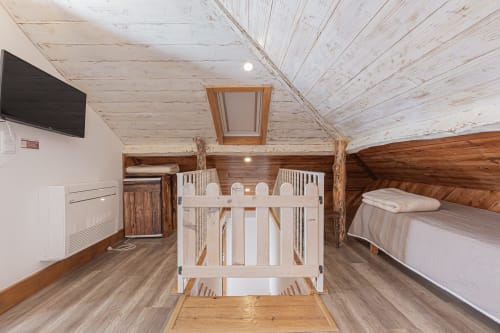 Rustic attic bedroom at Ninho Saloio with white crib, wooden beams, TV, and hardwood floors in Venda do Pinheiro