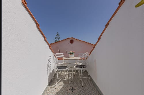 Narrow terracotta-roofed patio with white metal chairs at small table, Ninho Saloio hotel in Venda do Pinheiro