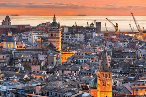 Tramonto dorato sul panorama storico di Genova con cattedrale a cupola e gru nel porto