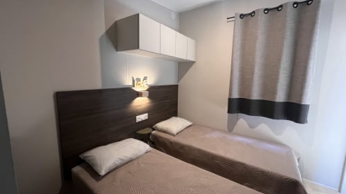 Deux lits jumeaux à tête de lit en bois foncé dans la chambre du Mobil-Home Yuka au Maquis Plage, Poggio-Mezzana