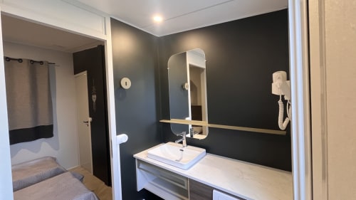 Salle de bain moderne du Mobil-Home Yuka Le Maquis Plage aux murs foncés, vasque blanche, miroir et sèche-cheveux à Poggio-Mezzana