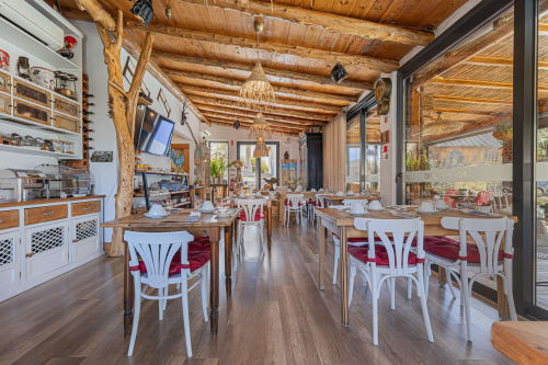 Sala de jantar rústica no Ninho Saloio com vigas de madeira, cadeiras brancas, almofadas vermelhas e vistas para o terraço em Venda do Pinheiro
