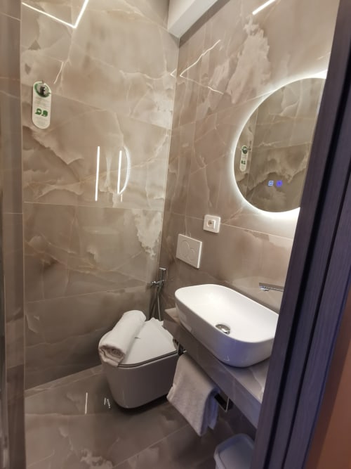 Bagno moderno dell'Hotel Fiori Roma con specchio illuminato, lavabo a bacinella, toilet e piastrelle effetto marmo
