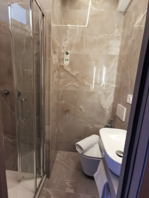 Bagno moderno dell'Hotel Fiori Roma con doccia walk-in in vetro, wc bianco, asciugamani e piastrelle neutre