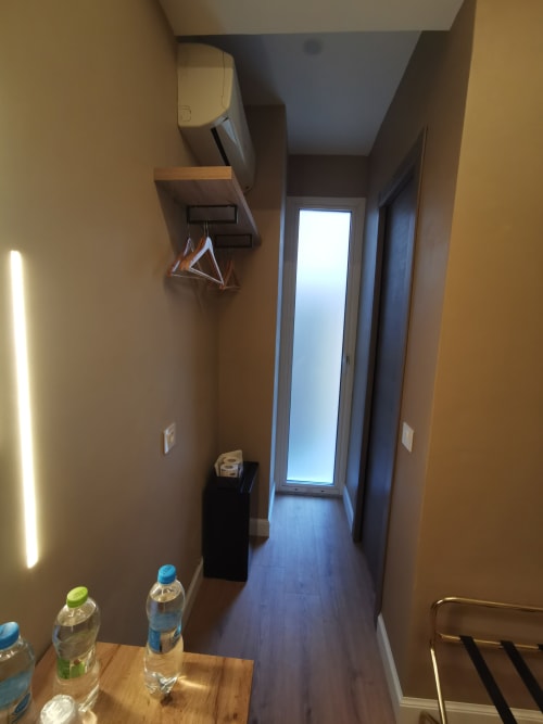 Stretto corridoio nella camera singola dell'Hotel Fiori Rome con pavimento in legno, illuminazione LED brillante e porta al balcone con vista sulla città