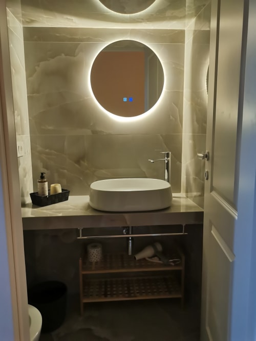 Bagno moderno all'Hotel Fiori Roma con specchio rotondo illuminato, lavabo bianco a coppa e pareti rivestite in marmo