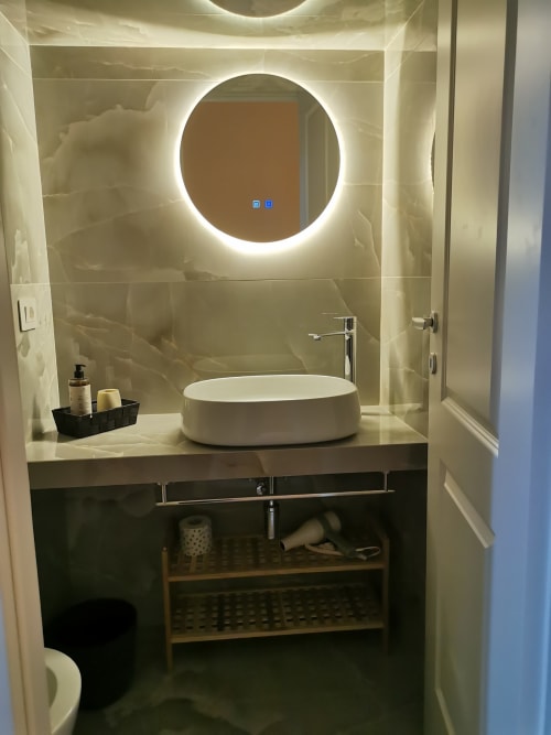 Bagno moderno all'Hotel Fiori Roma con specchio circolare illuminato, lavabo bianco in ceramica e mobile nero con vani di archiviazione