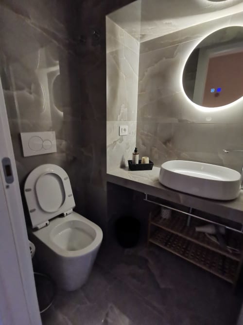 Bagno moderno dell'Hotel Fiori Roma con toilette bianca, lavabo ovale, specchio illuminato e rivestimento in marmo scuro