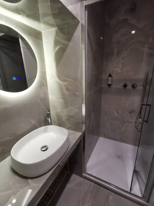 Bagno moderno dell'Hotel Fiori Roma con lavabo rotondo bianco, specchio illuminato e doccia walk-in con piastrelle grigie