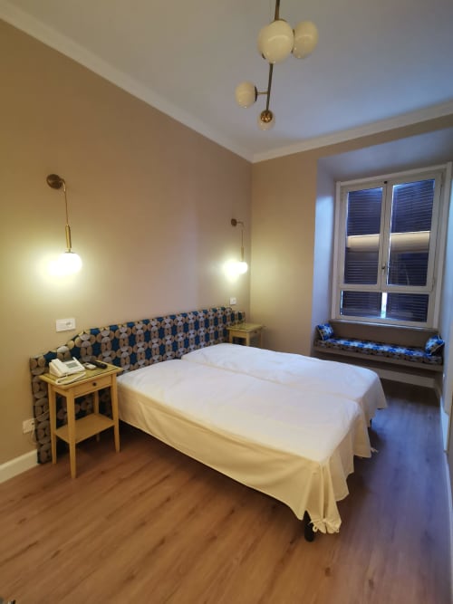 Camera doppia deluxe dell'Hotel Fiori Roma con pavimento in legno, testata decorata, illuminazione a sospensione e vista sulla città
