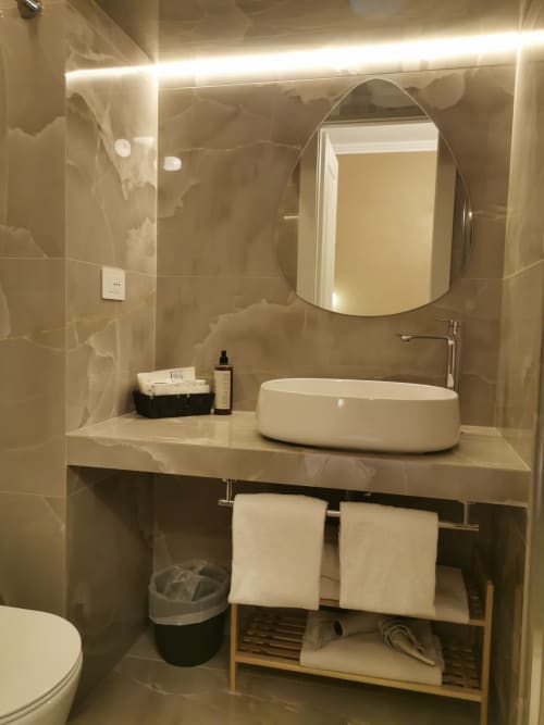 Bagno moderno dell'Hotel Fiori Roma con piastrelle in marmo, lavabo ovale, specchio illuminato e vanity organizzato con asciugamani