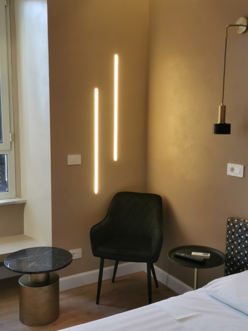 Angolo moderno di camera d'hotel con sedia nera, tavolino in marmo e luci neon illuminate alle pareti dell'Hotel Fiori, Roma.