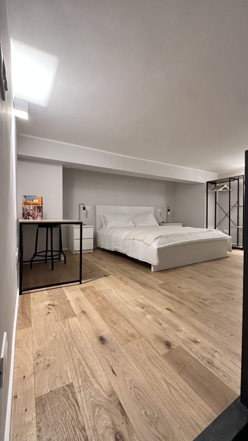 Camera moderna dell'hotel Pellicceria Superior a Genova con letto bianco, pavimento in legno, scrivania e arredamento minimalista