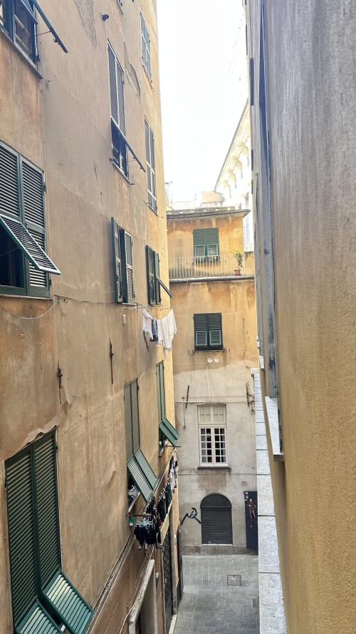 Stretto vicolo a Genova con edifici storici, persiane verdi e biancheria stesa tra le strutture di Pellicceria