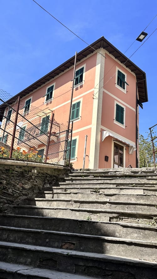 L'hotel Pellicceria Superior a Genova presenta un'affascinante facciata color rosa corallo con persiane verdi, accessibile da gradini in pietra