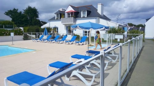 Loc'Maria Belle Île : Espace piscine avec chaises longues bleues, parasol et élégante demeure blanche surplombant la terrasse à Locmaria