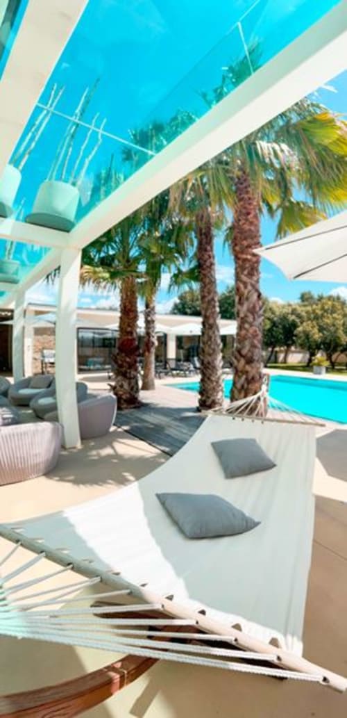 La Maison D'ambrine, salon au bord de la piscine avec palmiers, pergola blanche et piscine turquoise à Chamaret