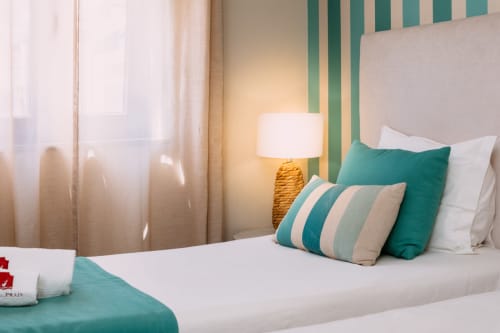 Quarto aconchegante na Casa da Praia com parede de destaque em tons de azul-petróleo, cama branca e almofadas decorativas em Zambujeira do Mar
