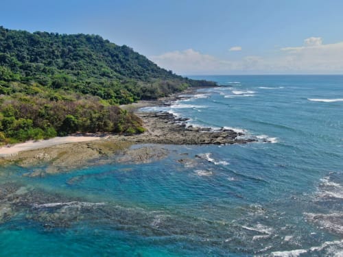 Pristine coastal cove at Organica Yoga Shelter in Paquera, Puntarenas with turquoise waters and lush jungle hillside