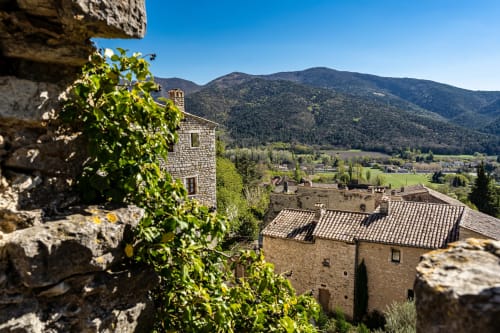 La Maison D'ambrine B&B domine la vallée de Chamaret avec ses bâtiments en pierre, vignes verdoyantes et montagnes boisées sous un ciel bleu