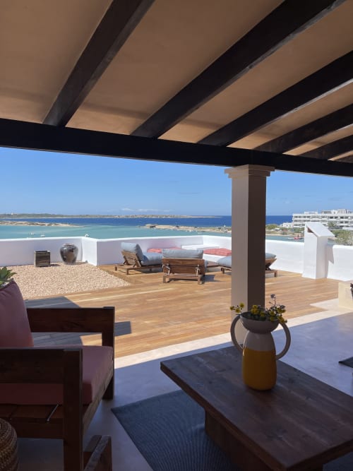 Terraza de apartamento en Formentera con vista al mar, tarima de madera, pérgola, tumbonas y aguas turquesas del Mediterráneo