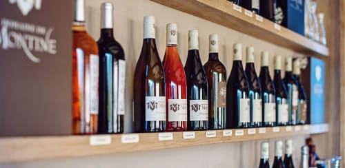 Wine bottles displayed on wooden shelf at La Maison D'ambrine boutique in Chamaret, France