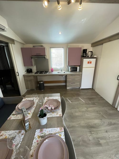 Studio moderne au Camping La Lézardière avec table à manger, cuisine, mobilier rose et coin salon