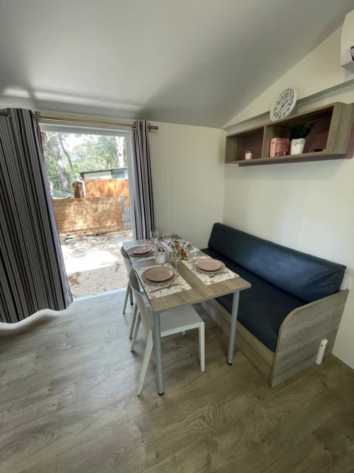 Chambre d'hôtel moderne au Camping La Lézardière avec table à manger, sièges noirs, étagères murales et portes vitrées donnant sur