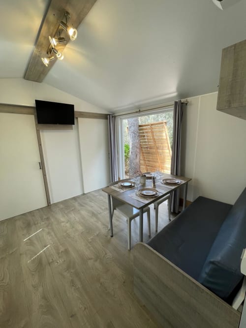 Coin repas moderne du mobil-home La Lézardière avec table, TV et vue montagne par la fenêtre