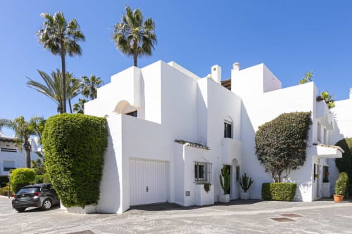 White modern beachside townhouse in Marbella with palm trees, green hedges, garage, and garden patio