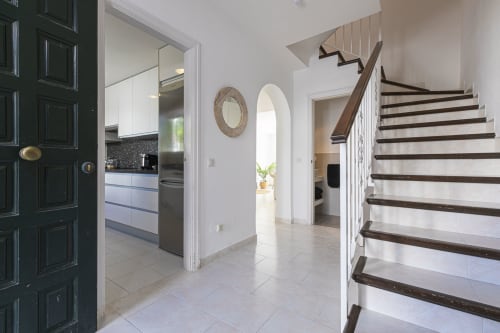 Modern Marbella townhouse entryway with black door, white staircase, and open-plan kitchen with dark countertops