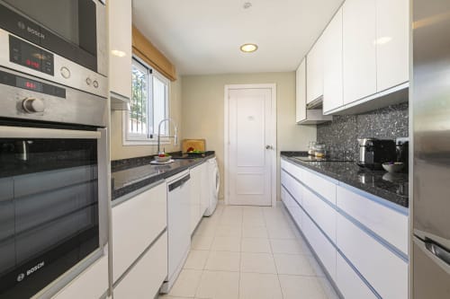 Modern white kitchen in Marbella townhouse with Bosch appliances, dark granite countertops, and stainless steel fixtures