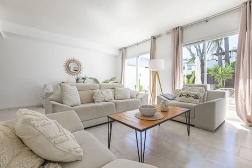 Bright modern living room with cream sofas, wooden coffee table, and garden views at Marbella beachside townhouse