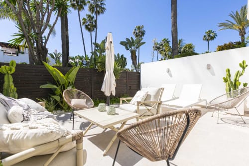 Luxury patio at Marbella beachside townhouse with lounge chairs, umbrella, white walls, palm trees, and garden view